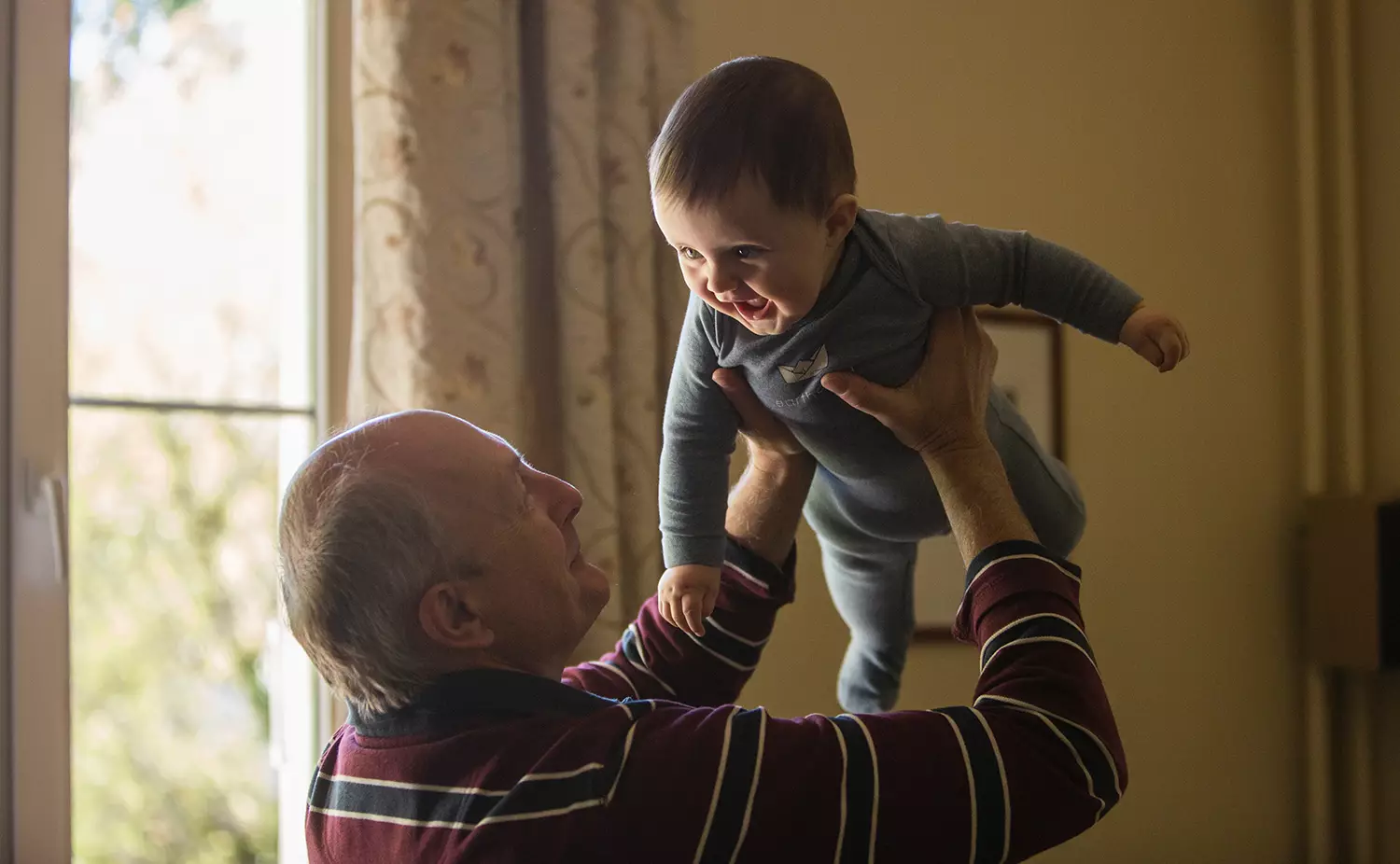 Avô levantando bebê que sorri de volta - Just Real Moms